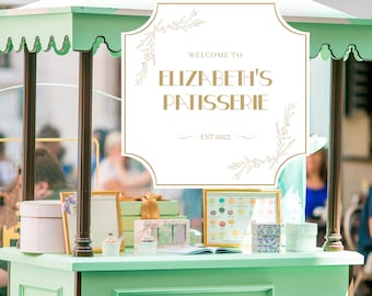 May include: A green and white pastry cart with a sign that reads "Welcome to Elizabeth's Patisserie Est 2023". The cart is decorated with gold accents and has a variety of pastries and boxes on display.