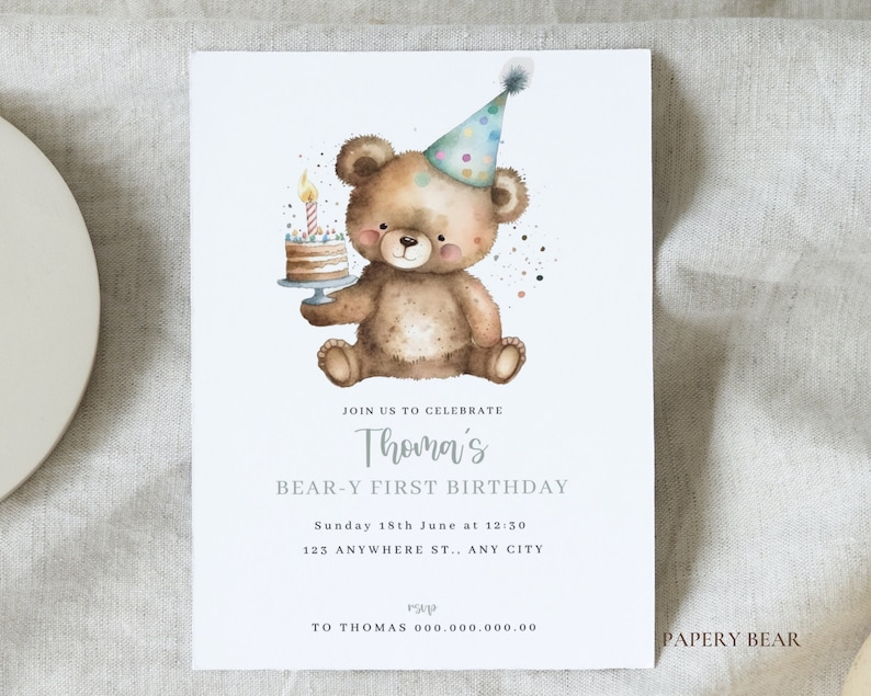 May include: A watercolor illustration of a brown teddy bear wearing a colorful party hat and holding a birthday cake with a lit candle. The text on the invitation reads "Join us to celebrate Thomas' Bear-y First Birthday. Sunday 18th June at 12:30. 123 Anywhere St., Any City. To Thomas 000.000.000.00. Papery Bear."