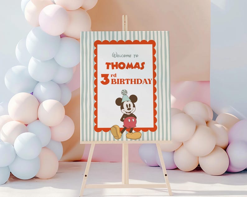Puede incluir: Un caballete de madera exhibe un letrero con el texto "Welcome to THOMAS 3rd BIRTHDAY". El letrero presenta un borde rojo festoneado, rayas verticales y un dibujo animado de Mickey Mouse. Globos pastel en rosa, blanco y azul decoran el fondo.