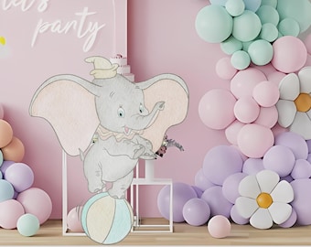 May include: A whimsical party scene featuring a Dumbo the elephant illustration balancing on a ball. Pastel balloons in pink, purple, and mint green create a festive backdrop. The words "let's party" are written in cursive on the wall.