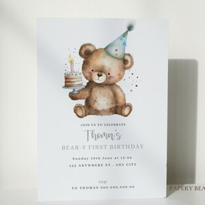 May include: A birthday invitation featuring a watercolor illustration of a brown teddy bear wearing a party hat and holding a birthday cake with a lit candle. The text on the invitation reads "Join us to celebrate Thoma's Bear-Y First Birthday, Sunday 18th June at 12:30, 123 Anywhere St., Any City, rsvp to Thomas 000.000.000.00, Papery Bear".