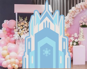 Puede incluir: Decoración de fiesta en forma de castillo azul claro con diseño de copo de nieve. El fondo incluye globos rosas y amarillos, arreglos florales y un arco rosa, creando un ambiente festivo.