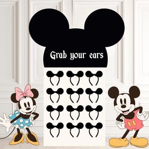 Puede incluir: Una exhibición con una gran forma de cabeza de Mickey Mouse negra y el texto "Grab your ears". Debajo hay 12 diademas negras con orejas de ratón. Los personajes de dibujos animados de Minnie y Mickey Mouse están a cada lado.