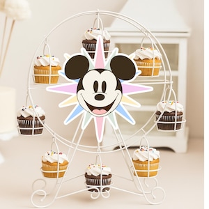 May include: A white metal Ferris wheel cupcake stand with eight cupcakes. The cupcakes are in wire baskets, alternating between yellow and chocolate cake, topped with white frosting and sprinkles. A Mickey Mouse cutout is in the center.