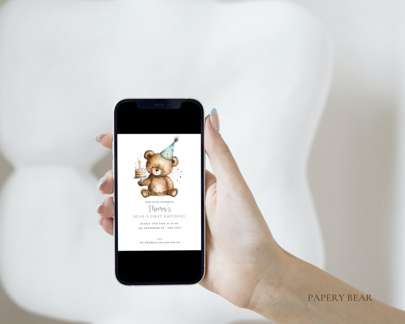 May include: A digital invitation for a first birthday party with a watercolor illustration of a brown bear wearing a blue and white party hat and holding a small cake with a single candle. The text on the invitation reads "Thomas's First Birthday".