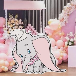 Puede incluir: Recorte de Dumbo el elefante, gris con orejas rosas y un collar rosa, frente a un telón de fondo rosa y blanco para una fiesta. El fondo incluye globos, flores y una mesa de postres, creando un ambiente festivo.