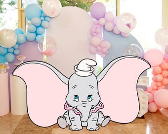 May include: A cartoon illustration of Dumbo the elephant with large pink ears, wearing a white hat and a pink collar. The background features pastel-colored balloons, creating a festive atmosphere, suitable for a baby shower or birthday party.