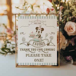 Könnte beinhalten: Ein gerahmtes Schild mit goldenem Rand zeigt eine Cartoon-Figur von Mickey Mouse, die einen Kuchen hält. Auf dem Schild steht oben "Sweet Store" und auf einem Banner "Favors". Darunter steht "Thank you for coming, Please take one!"