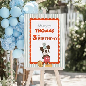 Puede incluir: Un letrero de bienvenida para el 3er cumplea&ntilde;os de Thomas, con Mickey Mouse. El letrero tiene un borde rojo festoneado y un fondo a rayas. Globos y flores decoran el fondo.