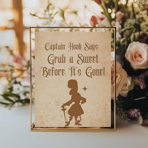 Könnte beinhalten: Ein goldgerahmtes Schild mit dem Text "Captain Hook Says: Grab a Sweet Before It's Gone!" in einer Vintage-Schriftart. Eine Silhouette einer Figur mit Schwert befindet sich darunter. Der Hintergrund ist beige.