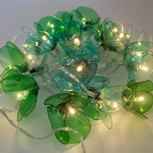 Peut inclure: Une guirlande lumineuse avec des ampoules en forme de fleur en plastique vert et bleu. Les lumières sont reliées par un fil transparent.