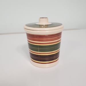 May include: A ceramic jar with a lid, featuring a striped design in shades of brown, green, and yellow.