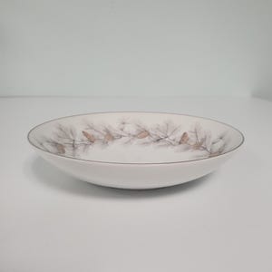 May include: A white ceramic bowl with a brown and gray pine cone design around the rim.
