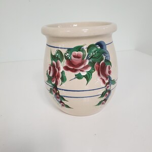 May include: A white ceramic vase with a blue and white striped design and hand-painted pink roses with green leaves.