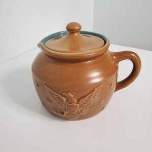 May include: A brown ceramic pitcher with a blue lid and a raised design of an eagle with stars.