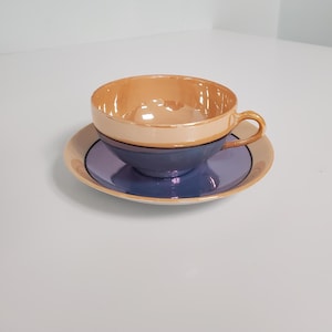 May include: A vintage teacup and saucer set. The teacup is peach-colored on top and transitions to a deep blue. The saucer is peach with a blue center. The set is likely made of ceramic or porcelain.
