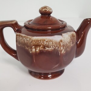 May include: A small brown and white ceramic teapot with a lid. The teapot has a mottled glaze with brown and white swirls.
