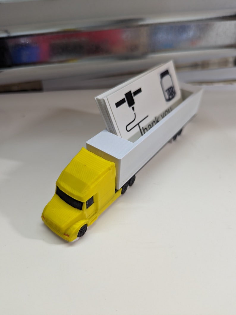 May include: A yellow toy semi-truck with a white trailer. The trailer is holding a stack of business cards with the text "Thank you" printed on them.