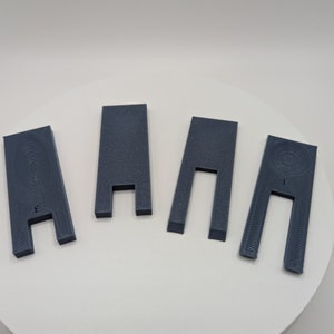 May include: Four gray plastic spacers with different sized openings. The spacers are designed to fit between two surfaces to create a gap.