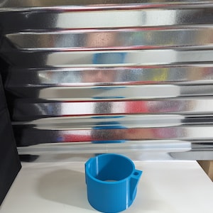 Op de afbeelding: Een felblauw cilindrisch onderdeel met een gladde afwerking, voorzien van een verticale zijbevestiging met een klein rond gat. Het object heeft een hol midden en een uniforme wanddikte, met duidelijk zichtbare 3D-geprinte laaglijnen.