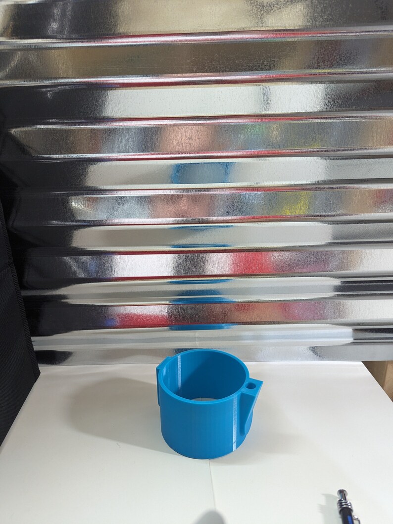 Op de afbeelding: Een felblauw cilindrisch onderdeel met een gladde afwerking, voorzien van een verticale zijbevestiging met een klein rond gat. Het object heeft een hol midden en een uniforme wanddikte, met duidelijk zichtbare 3D-geprinte laaglijnen.