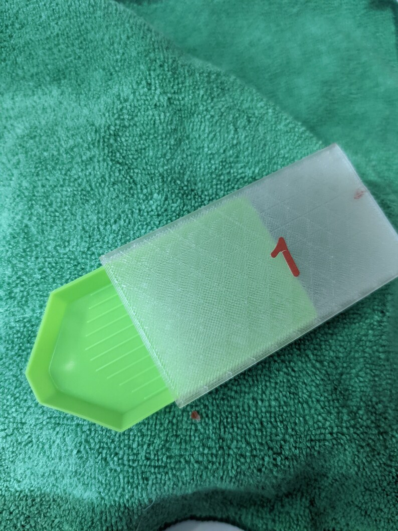 Puede incluir: Una bandeja de pintura de diamantes verde con una tapa de pl&aacute;stico transparente etiquetada con el n&uacute;mero "1".