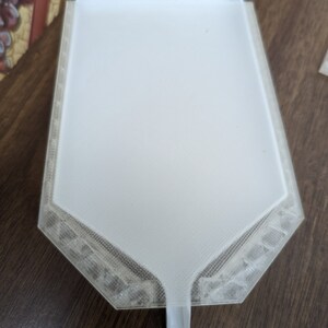 Puede incluir: Un embudo de pl&aacute;stico blanco con una base hexagonal y un pico. El embudo est&aacute; dise&ntilde;ado para verter l&iacute;quidos en recipientes con aberturas estrechas.