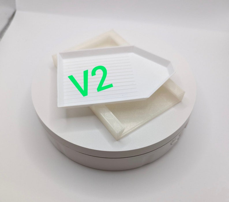 Puede incluir: Bandeja de pintura de diamantes blanca con una base giratoria blanca. La bandeja tiene una superficie texturizada y el texto "V2" est&aacute; impreso en la bandeja.