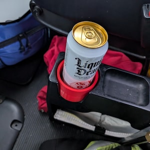 May include: A can of Liquid Death Mountain Water in a red cup holder. The can is silver with a gold top and black text that reads "Liquid Death Mountain Water".