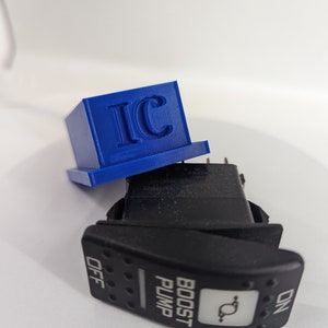 May include: A black toggle switch with the words "BOOST PUMP" and "ON" and "OFF" printed on it. The switch is sitting on a white surface with a blue plastic box with the letters "IC" printed on it.