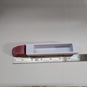 May include: A white plastic model truck bed with a red cab. The truck bed is 7 inches long and the cab is 1.5 inches long. The model is sitting on a white surface with a ruler next to it.