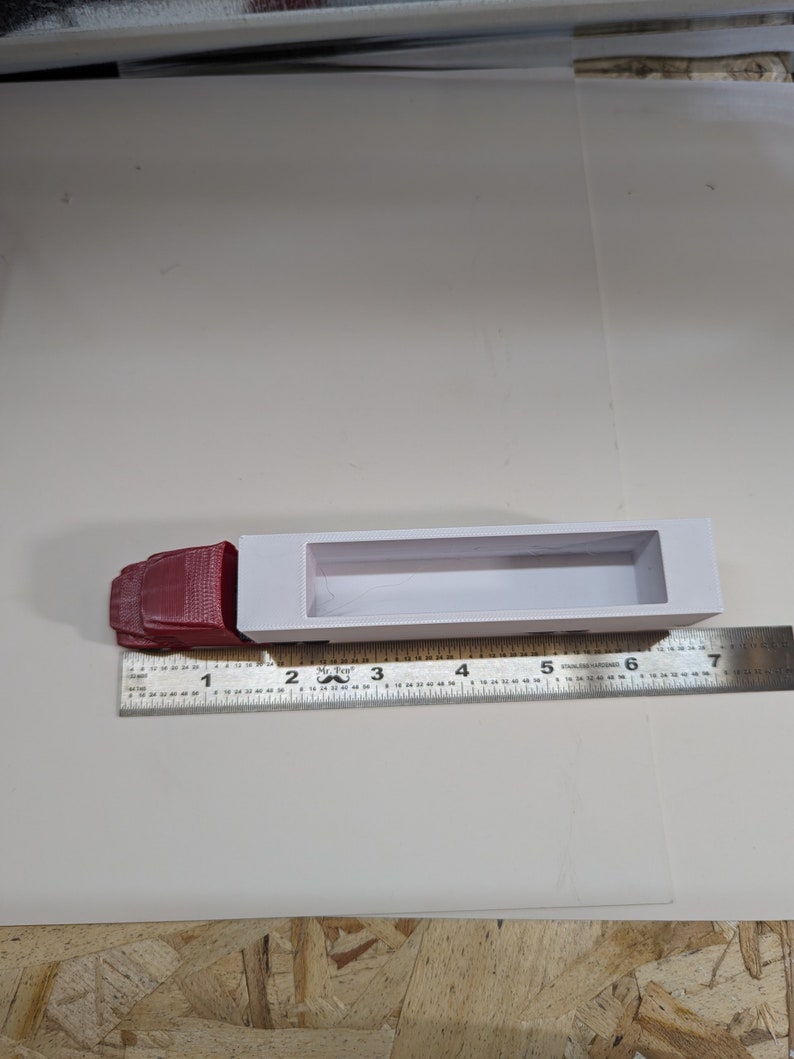 May include: A white plastic model truck bed with a red cab. The truck bed is 7 inches long and the cab is 1.5 inches long. The model is sitting on a white surface with a ruler next to it.