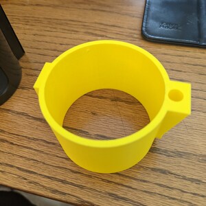 Op de afbeelding: Een felgele, cirkelvormige, 3D-geprinte kunststof ringcomponent met een platte, uitstekende lip aan &eacute;&eacute;n kant met een klein, gecentreerd cirkelvormig gat. Het object heeft een gladde, matte afwerking en een uniforme cilindrische wand.