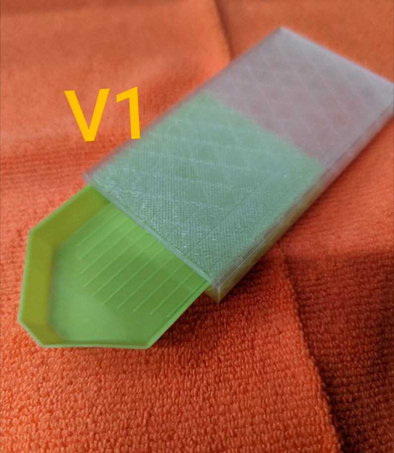 Puede incluir: Una bandeja de pintura de diamantes verde con una tapa de pl&aacute;stico transparente. La tapa tiene un patr&oacute;n de cuadr&iacute;cula y la bandeja tiene una superficie estriada. El texto "V1" es visible en la imagen.