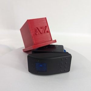 May include: A black rocker switch with a blue LED light. The switch is mounted on a red plastic base with the letters "AZ" printed on it.