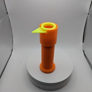 May include: An orange and yellow 3D printed tool with a ring at the top and a pointed tip. The tool is sitting on a white surface.