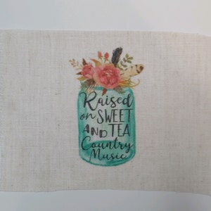 May include: A burlap fabric square with a printed design of a mason jar with flowers and the text "Raised on Sweet and Tea Country Music".