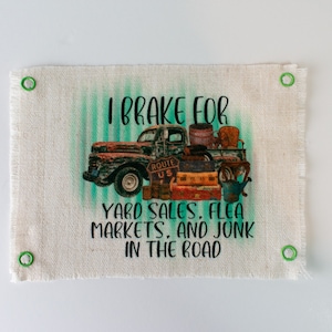 May include: A white canvas sign with green and blue stripes and a vintage truck image. The sign reads "I brake for yard sales, flea markets, and junk in the road".