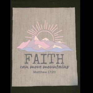 May include: A light gray fabric square with a graphic design featuring a pink and blue mountain range, a rising sun, and the words "FAITH can move mountains" with the Bible verse Matthew 17:20.