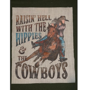 May include: A tan fabric with a graphic of a person riding a horse, wearing a cowboy hat and jeans. The text reads "Raisin' Hell With The Hippies & The Cowboys" in various fonts and colors.