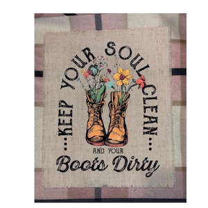 May include: A rustic-style graphic featuring two brown cowboy boots filled with colorful flowers. The text reads "...KEEP YOUR SOUL CLEAN...AND YOUR Boots Dirty" in a circular arrangement. The design is on a beige, textured background.