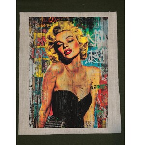 May include: A pop art style portrait of Marilyn Monroe with blonde hair and red lipstick. She wears a black strapless top. The background is a collage of graffiti and colorful paint splatters, with some text visible.