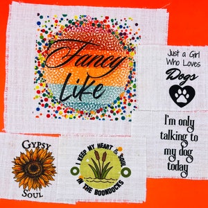 May include: Four fabric squares with different designs. The first square has a colorful background with the text "Fancy Like". The second square has the text "Just a Girl Who Loves Dogs" with a black paw print heart. The third square has the text "Gypsy Soul" with a sunflower. The fourth square has the text "I Keep My Heart & Soul In The Boondocks" with a green background and a drawing of cattails.