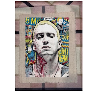 May include: A portrait of a man with blonde hair and a serious expression, with red streaks on his face and neck. The artwork includes the text "8 Mile" and other colorful graffiti-style elements. The image is on a canvas.