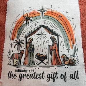 May include: A fabric patch featuring a Nativity scene with a rainbow arch. The illustration includes Mary, Joseph, baby Jesus, and two sheep. Text reads "Matthew 1:21" and "the greatest gift of all."