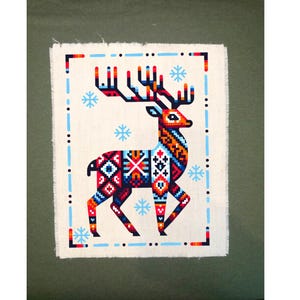 May include: A white fabric with a blue border and a red, orange, blue, and black patterned deer with antlers. The deer is surrounded by blue snowflakes.