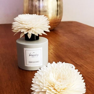 May include: A grey diffuser bottle with a white label that says "The bermondsey" and a white wooden flower on top. The bottle is sitting on a wooden surface.