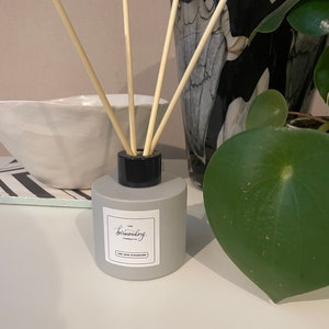 Könnte beinhalten: Eine graue Diffuserflasche mit schwarzem Deckel und Holzstäbchen. Die Flasche hat ein weißes Etikett mit dem Text "The Bermondsey Candle Co." und "Lime Basil & Mandarin".