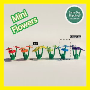 May include: A set of seven mini flower arrangements made of LEGO bricks. Each flower is a different color of the rainbow, starting with red and ending with purple. The flowers are 3.5 inches tall and are arranged in a row on a white surface. The text "Soda Can" is written above the flowers.