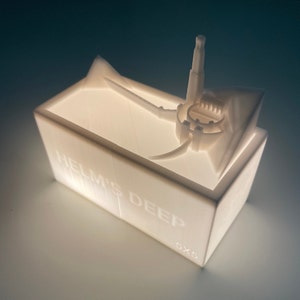 May include: White 3D printed model of Helm's Deep from the Lord of the Rings, with the text "Helm's Deep 5x5" on the base.